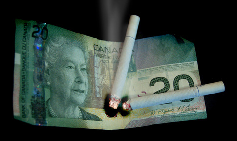 Picture of two lit cigarettes burning a hole through a twenty dollar bill.  Photo © 2011, FreePhotoCourse.com, all rights reserved  
